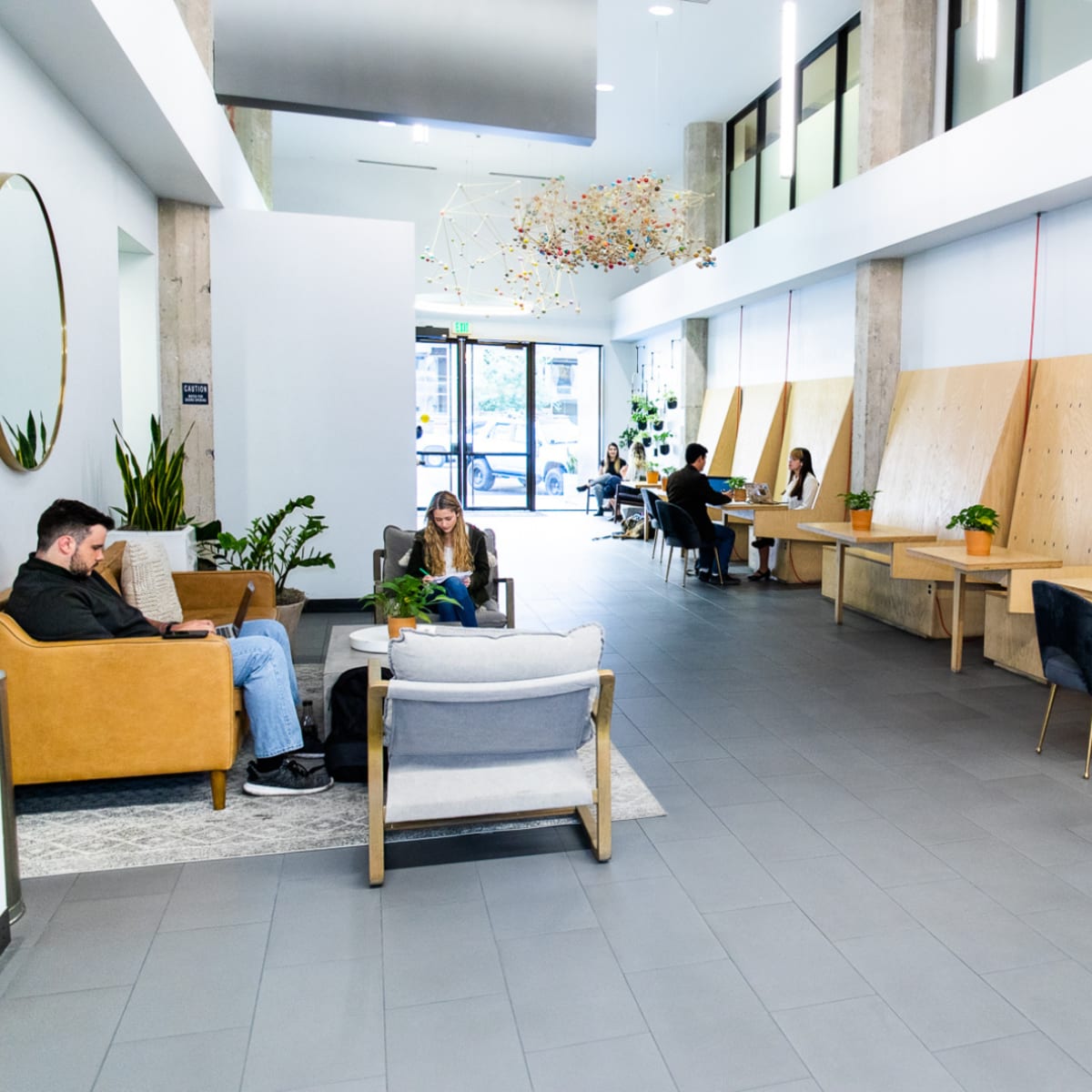 A spacious modern lobby with several seating areas, plants, and large windows letting in natural light.