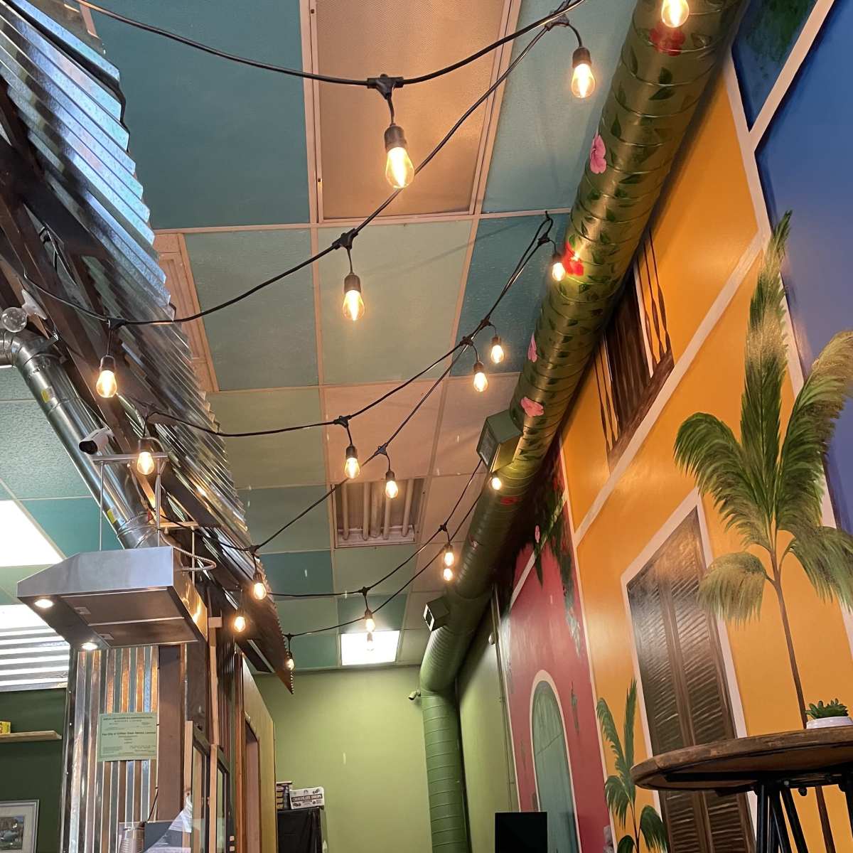 A brightly colored interior of a cafe, featuring string lights hanging from the ceiling and decorative murals on the walls.