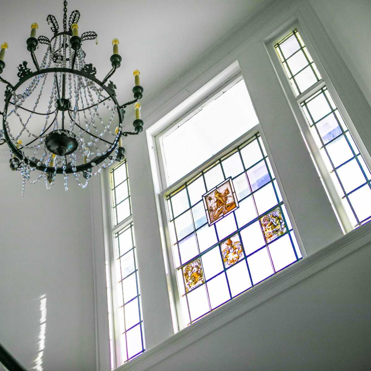 A staircase under a chandelier with stained glass windows illuminating the space.