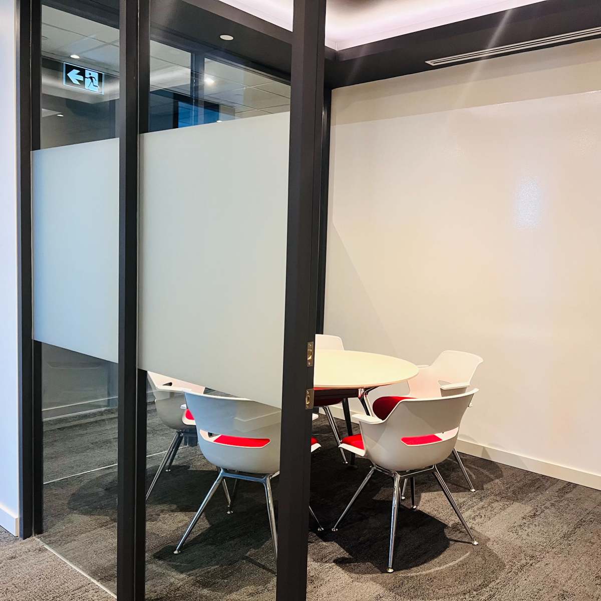 A small meeting room features a round table surrounded by white chairs with red accents.