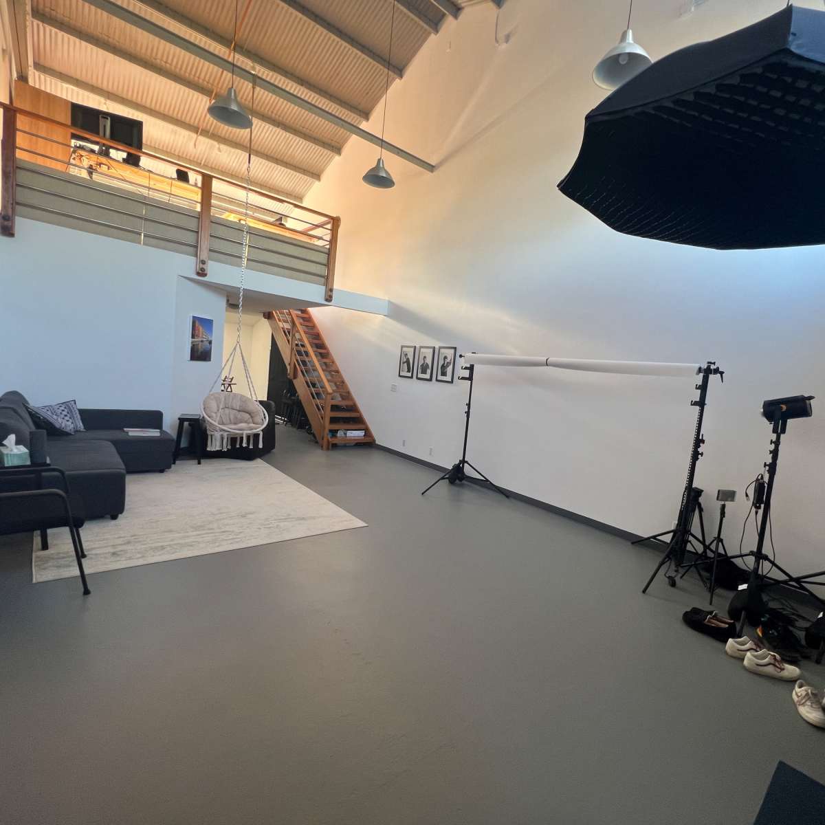 A spacious room with a couch, a rug, several lighting equipment stands, and a staircase leading to an upper level.
