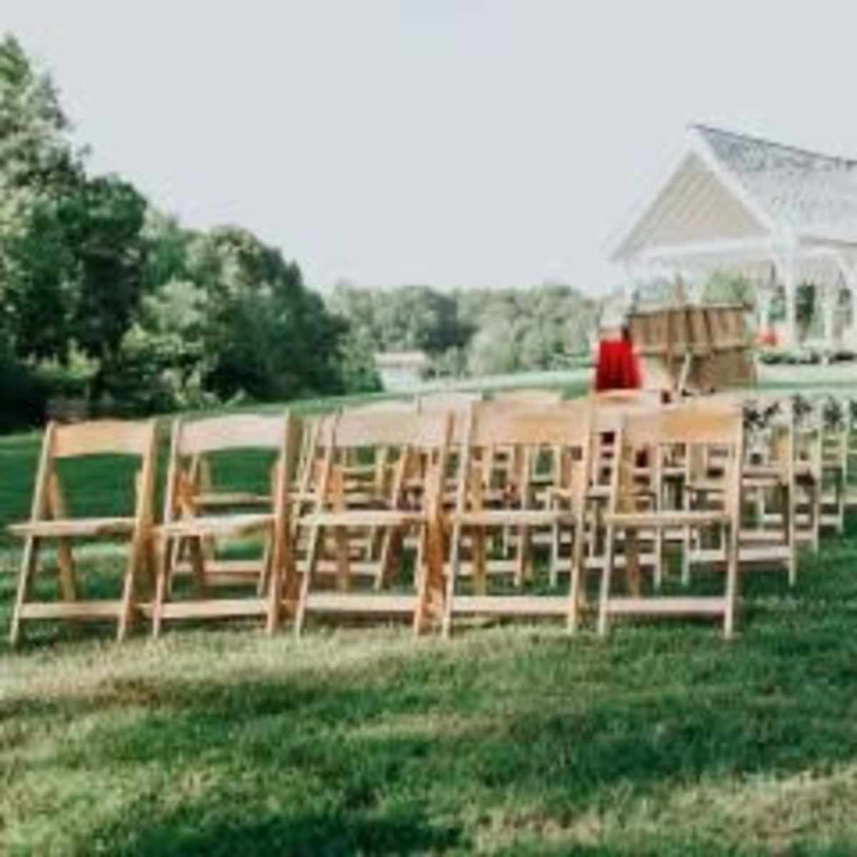 A set of wooden chairs is arranged in rows facing a decorated gazebo on a grassy field.