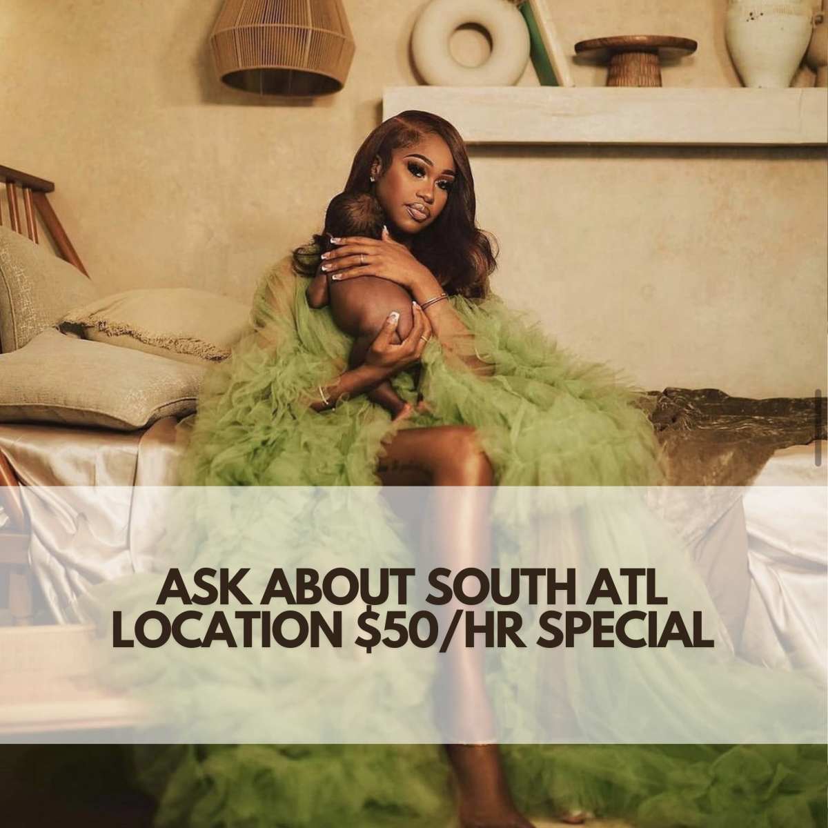 A person in a green fluffy outfit holds a baby while seated on a bed with a cozy, decorated room in the background.