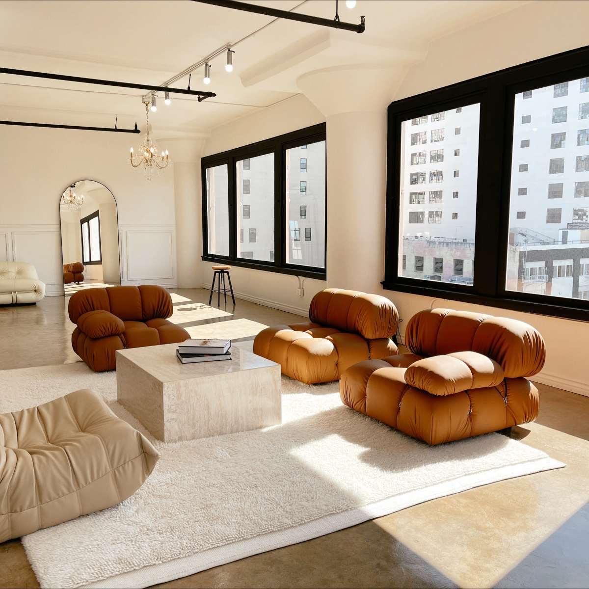 The spacious room features contemporary furniture, including a large coffee table and several uniquely shaped sofas, illuminated by natural light from large windows.