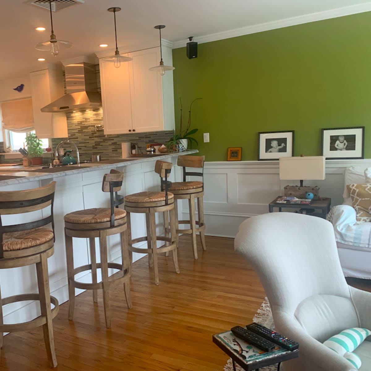 A modern kitchen with white cabinetry, a green accent wall, and four wooden bar stools positioned at a counter.