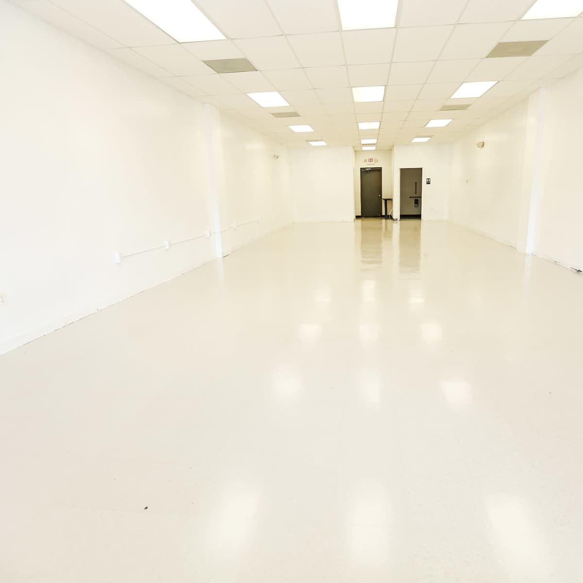 A large, empty room with white walls and a bright, glossy floor.
