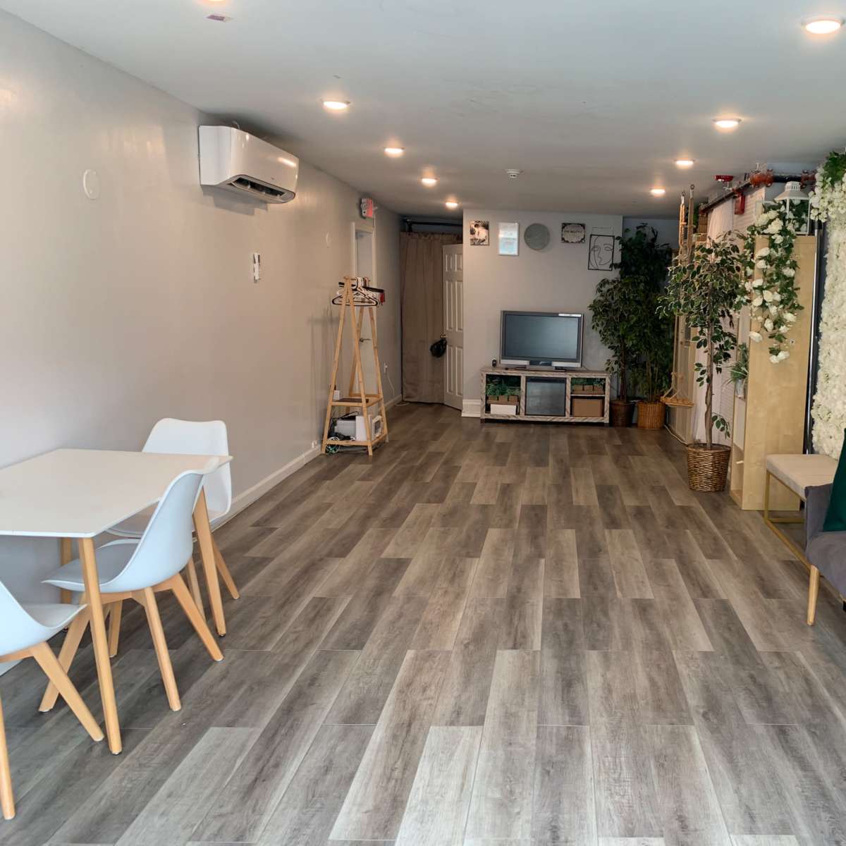 A modern interior space with a wooden floor, light walls, and various plants, including a green wall and decorative elements like a television and seating.