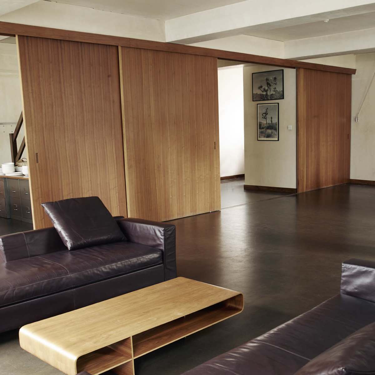 A modern, open-concept living space with leather sofas, a wooden coffee table, and sliding wood-panel doors leading to another room.