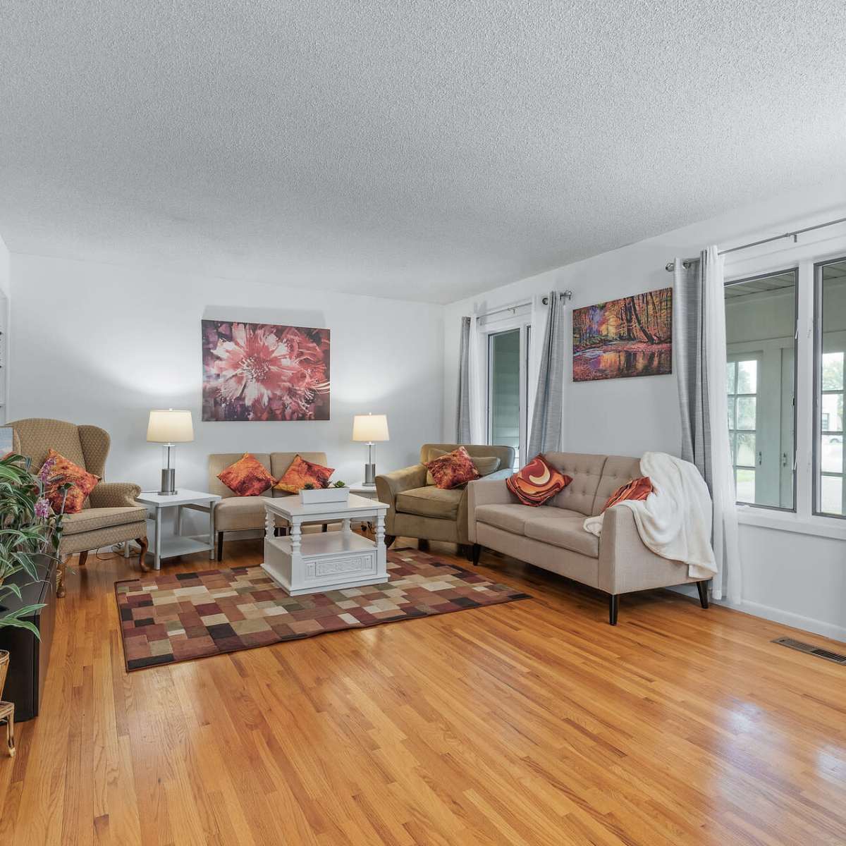 A living room with two sofas and an armchair, a coffee table, and artwork on the walls, all set on a hardwood floor with a patterned rug.