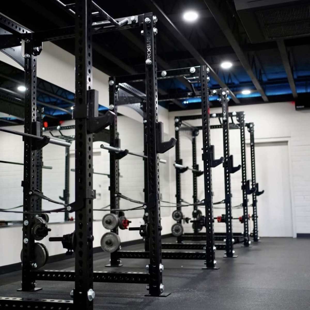 A row of black weightlifting racks arranged in a gym with a minimalist design.