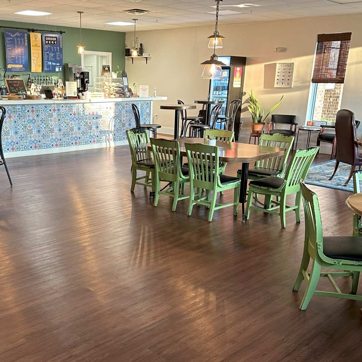 A cozy café interior with a counter displaying a menu and seating areas featuring green chairs and wooden tables.