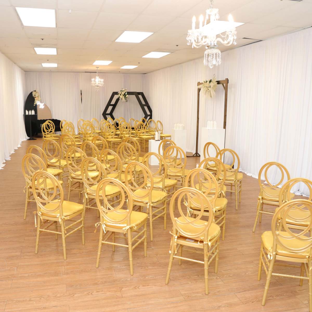 A spacious room set up with rows of gold chairs facing a decorated backdrop, surrounded by white drapery.