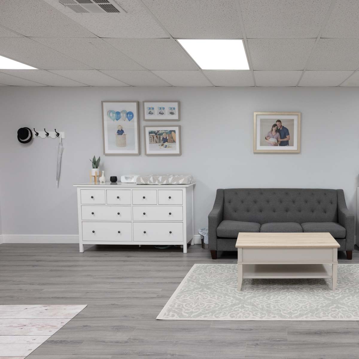 A modern, well-lit room with a gray sofa, a coffee table, and white furniture, including a dresser and a small refrigerator against the wall.