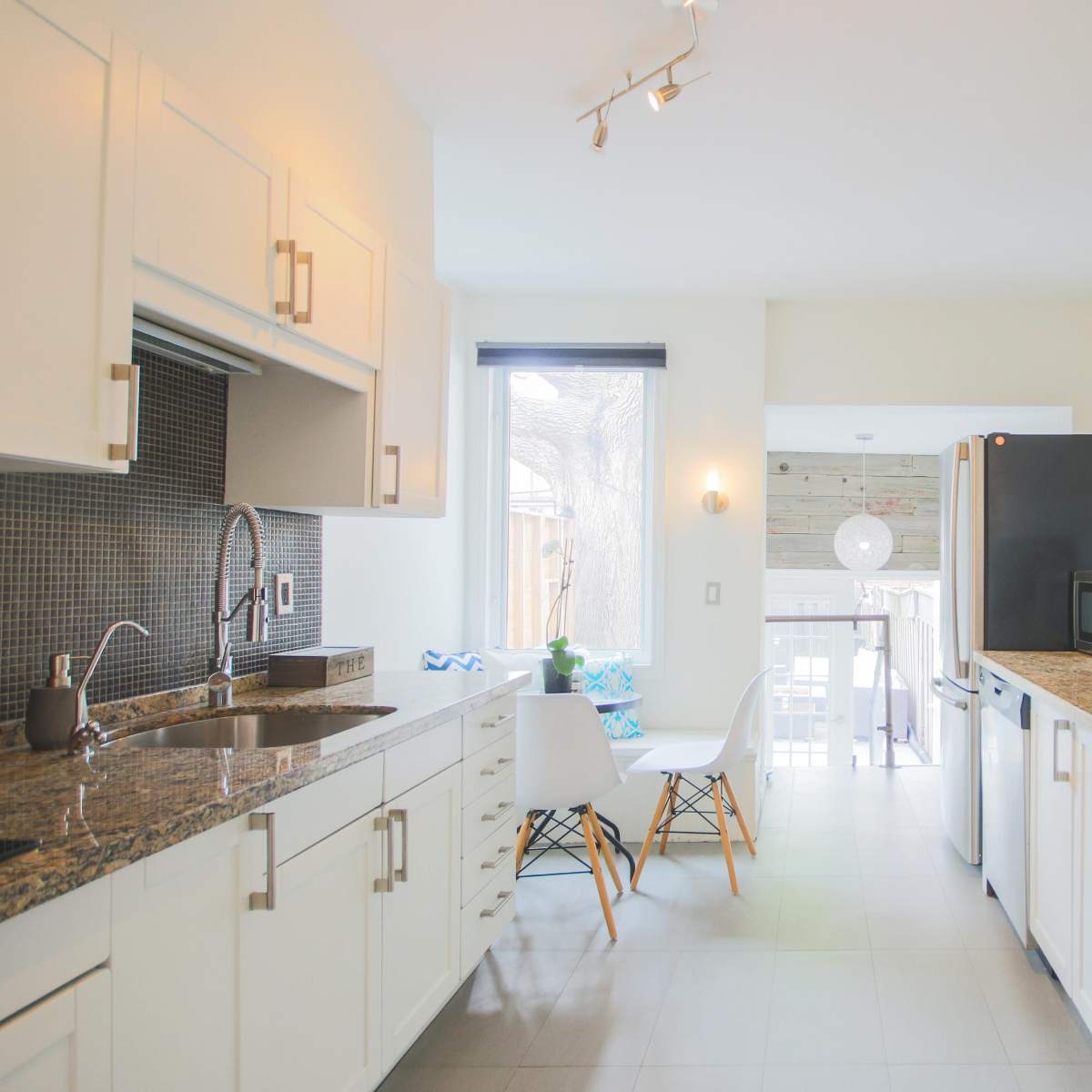 A bright kitchen features white cabinetry, granite countertops, and a dining area with a view of an outdoor space.