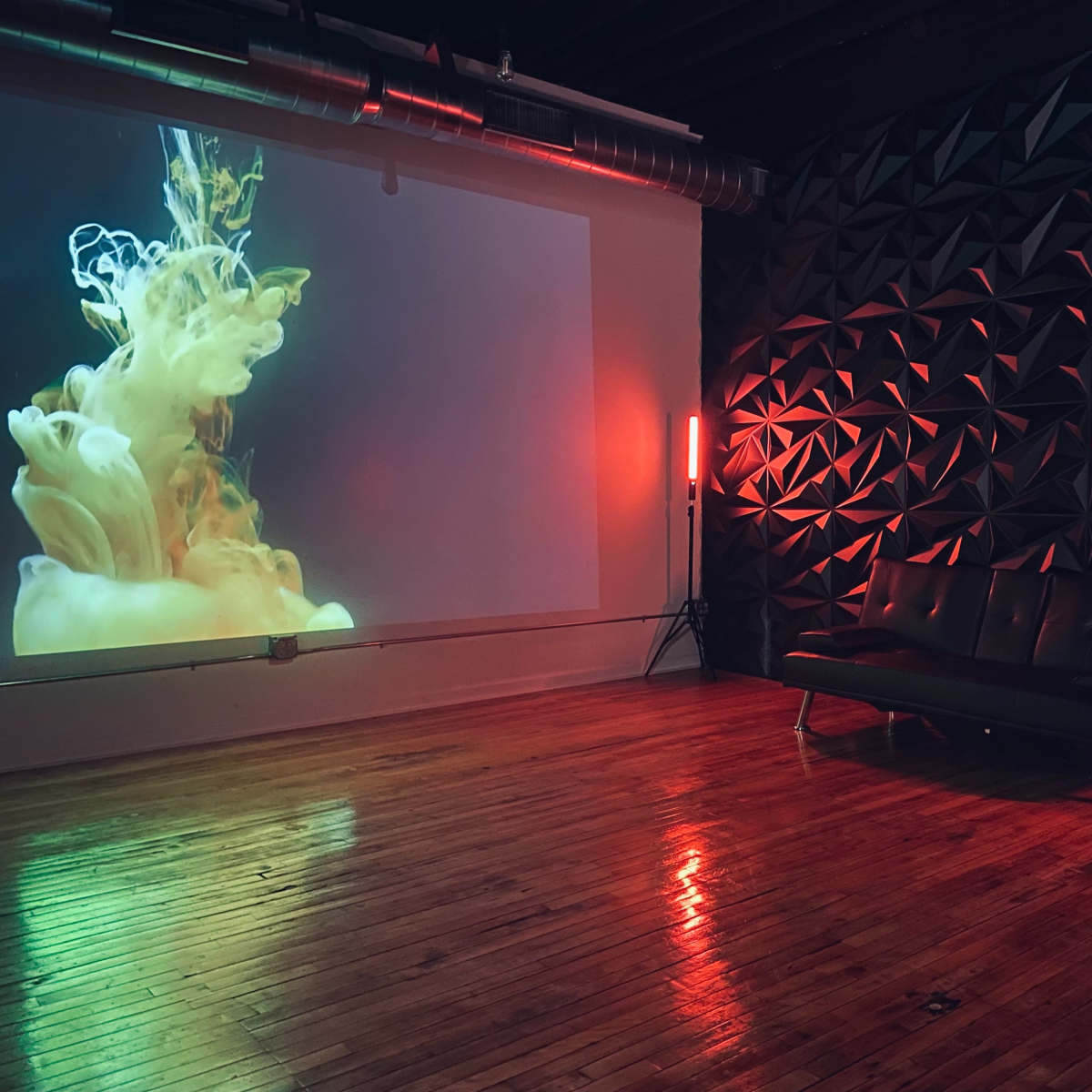 A modern room with a projected abstract colorful display on one wall and a black leather couch against a textured geometric wall.