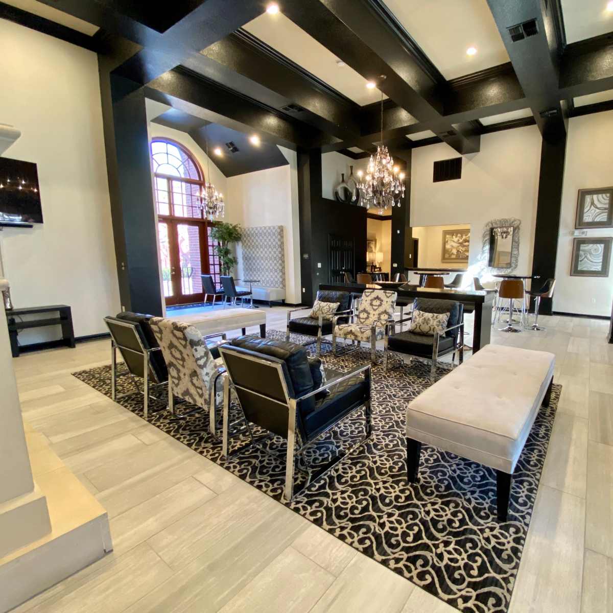 A spacious lounge area with black wooden beams, modern seating arrangements, and a large area rug featuring an intricate pattern.
