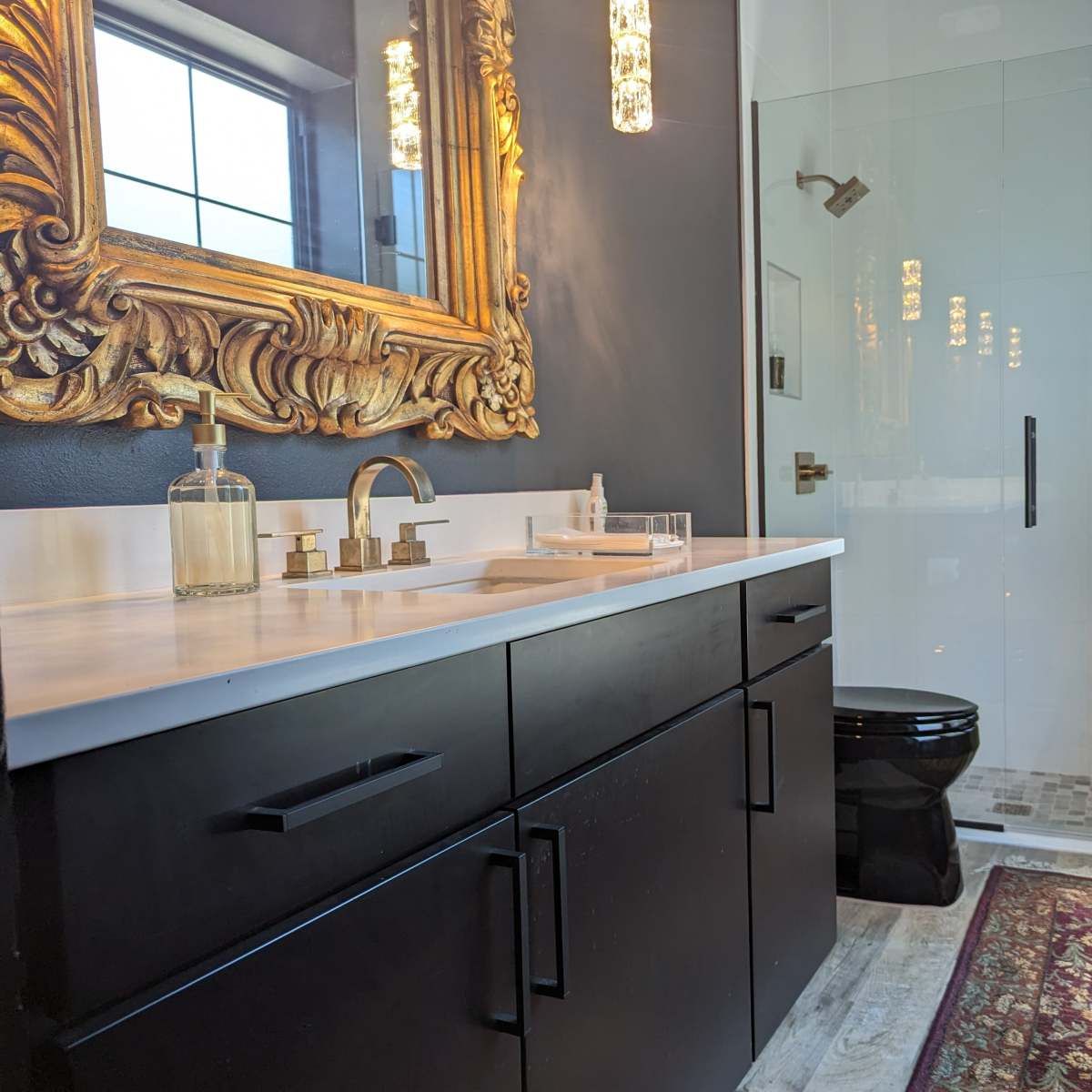 A modern bathroom featuring a black vanity with a marble countertop, a large ornate mirror, a glass shower enclosure, and a toilet.