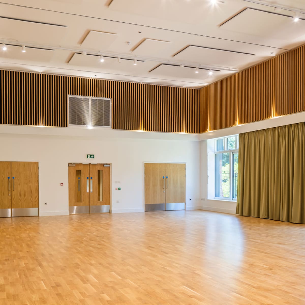A spacious room with wooden flooring, large windows, and a wall adorned with wooden slats, along with two sets of double doors.