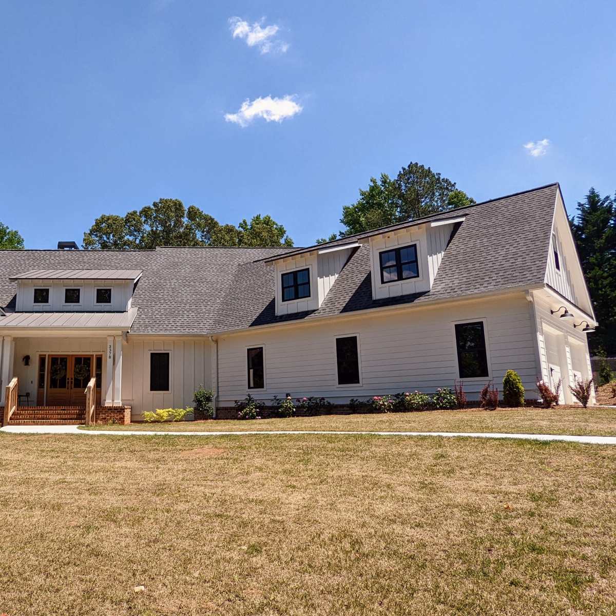 A large, modern white house with a gabled roof and multiple windows is situated on a grassy lot surrounded by trees.