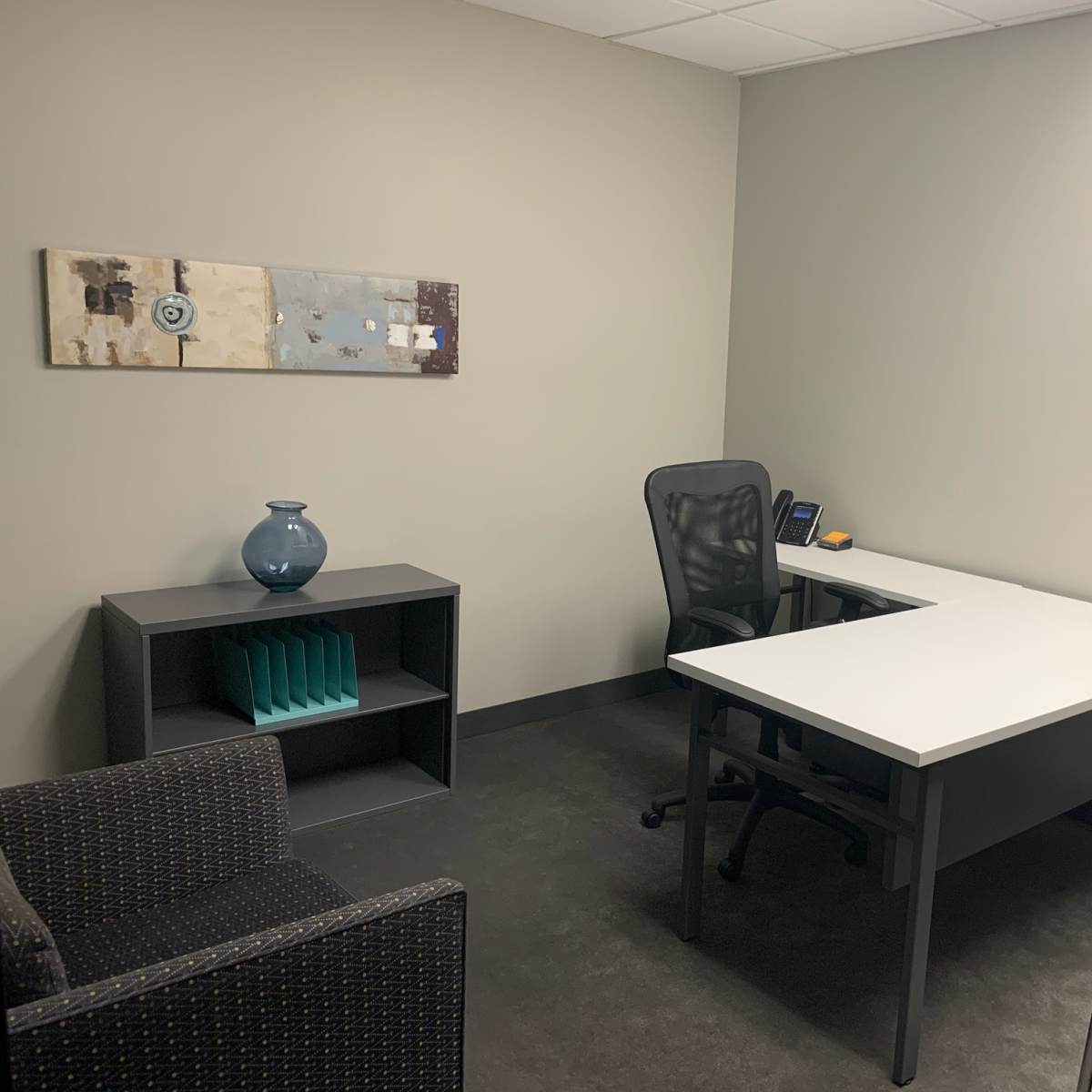 A small office space featuring a desk with a chair, a shelf with decorative items, and a couch in the corner.