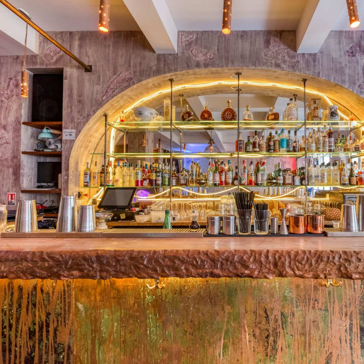 A well-stocked bar features an illuminated display of various bottles behind a polished countertop.