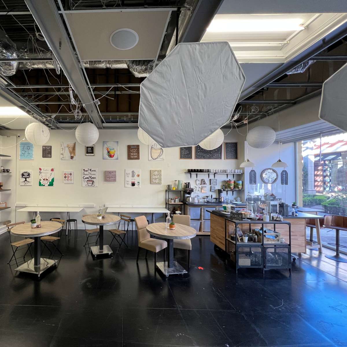 The interior of a café features wooden tables and chairs, a display shelf on the left, and decorative paper lanterns hanging from the ceiling.