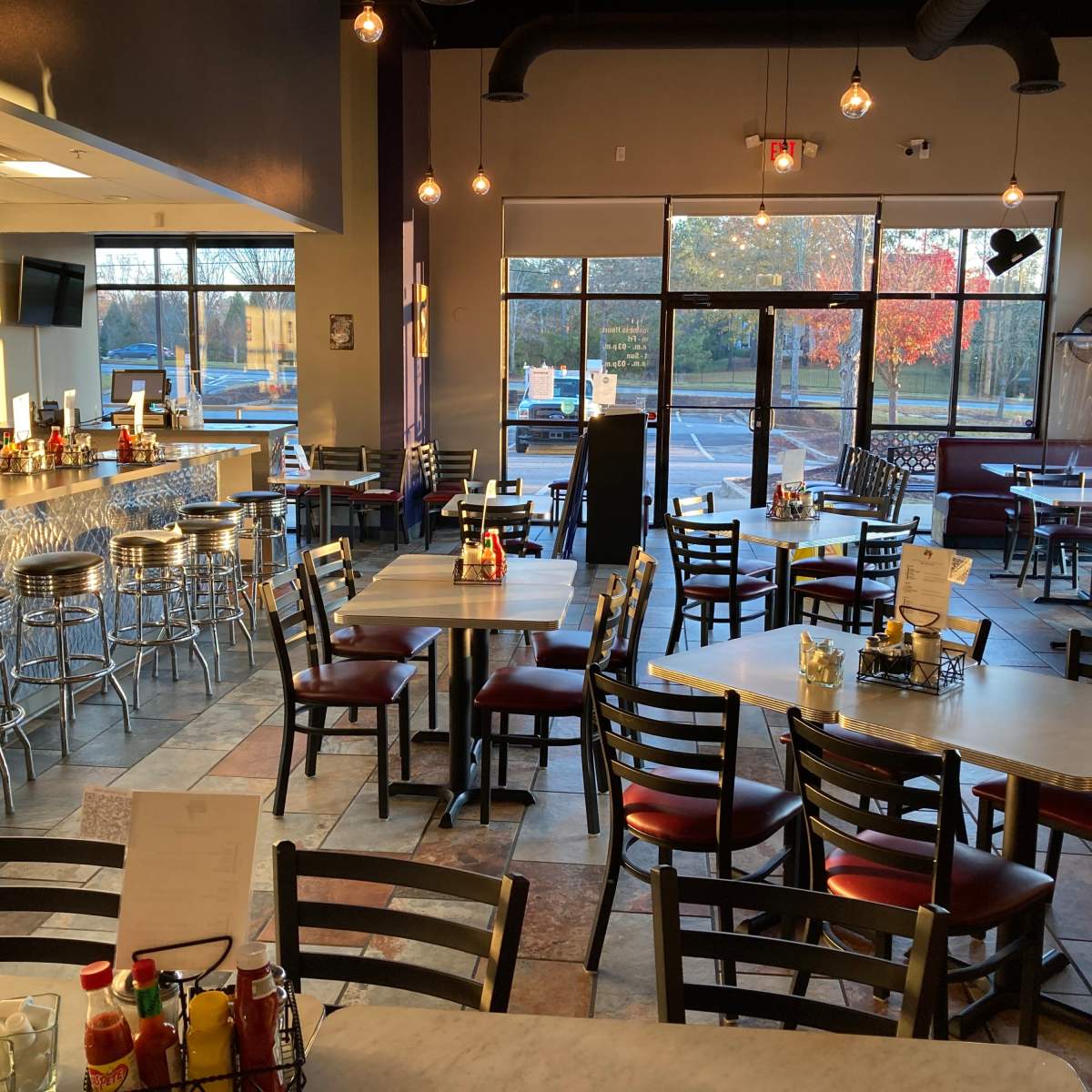 A modern restaurant interior with empty tables and chairs, a counter area, and large windows displaying an outdoor view.
