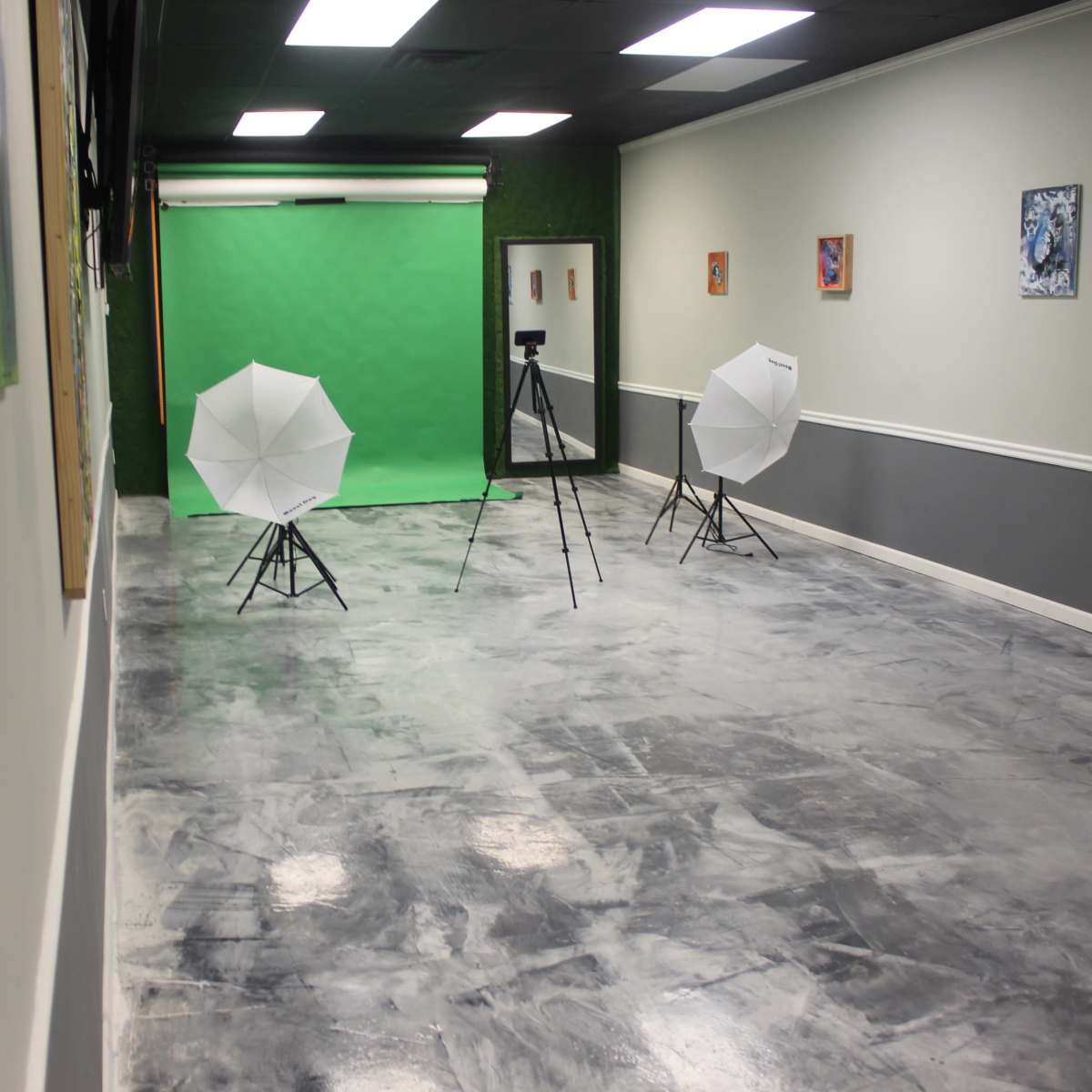 A photography studio with a green backdrop, two softbox lights on tripods, and a concrete floor.
