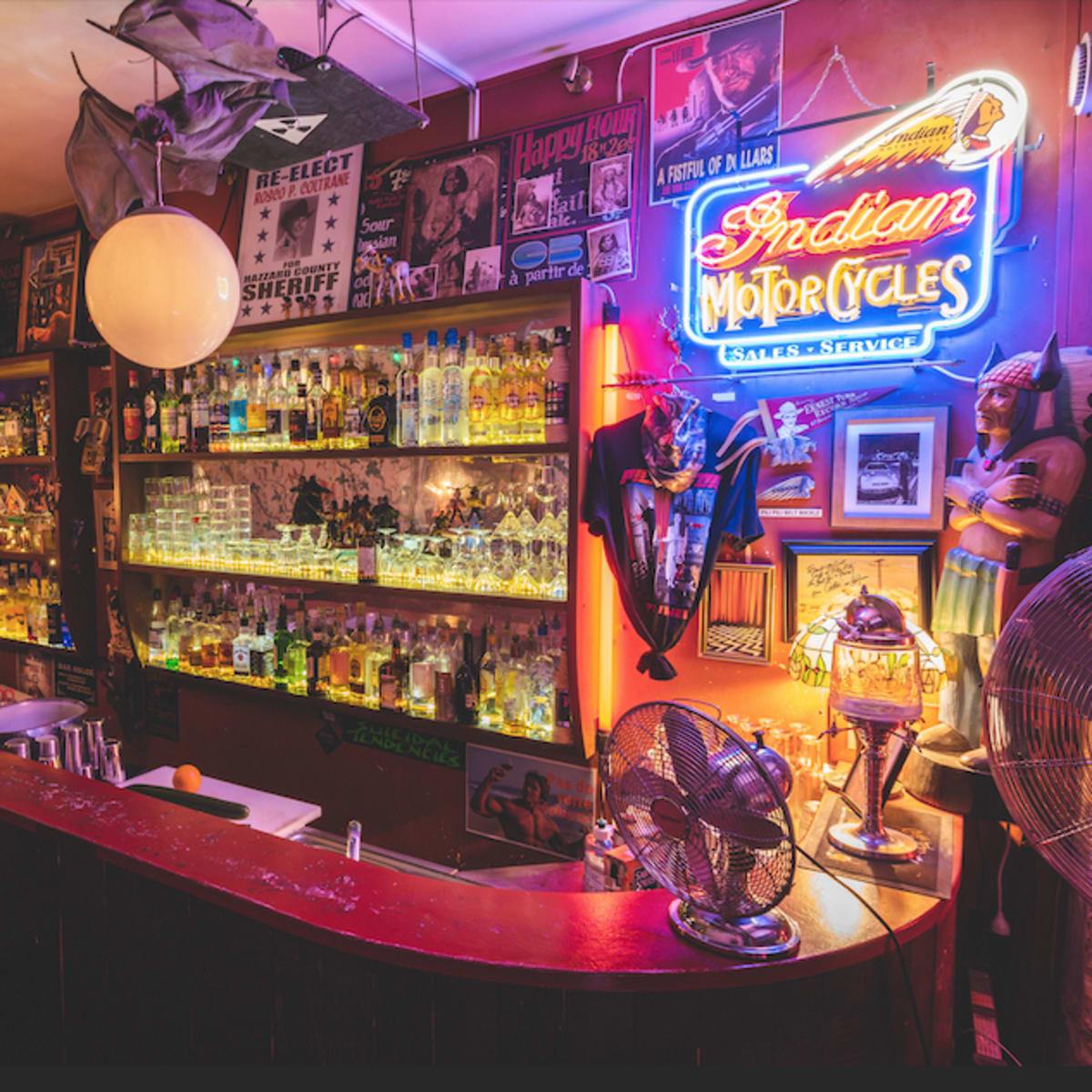 A dimly lit bar with a curved counter, shelves filled with bottles, and neon signage in a vibrant atmosphere.