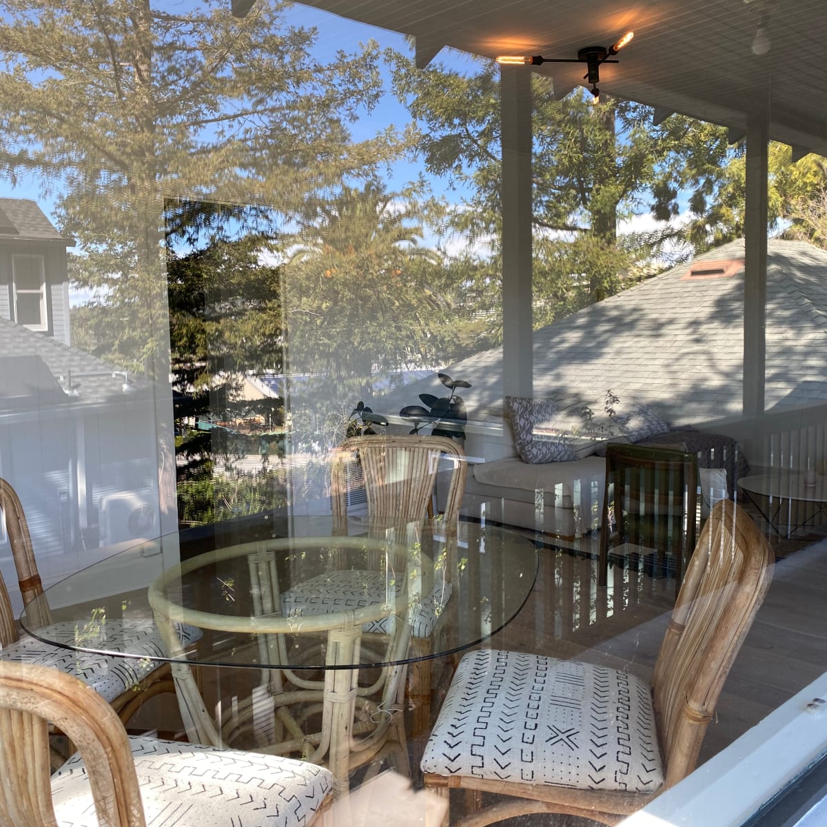 A glass-topped table with rattan chairs is visible on a porch, reflecting trees and the exterior of nearby houses.