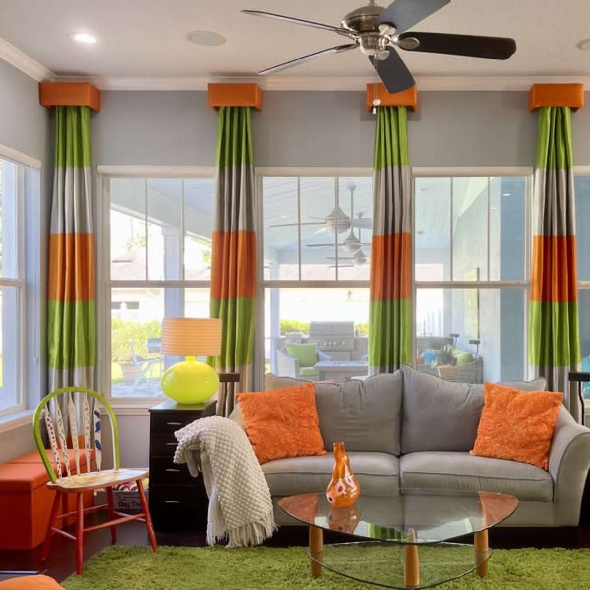The living room features a gray sofa, an orange accent chair, and colorful curtains with green, orange, and gray stripes, highlighted by a circular glass coffee table.