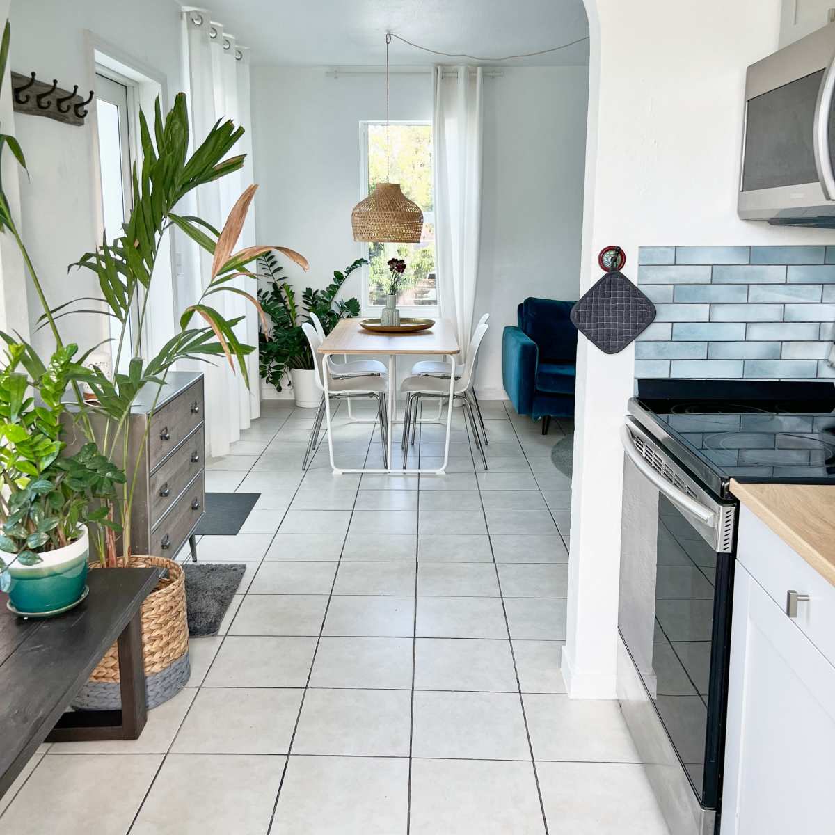 A bright kitchen features a white arch leading to a dining area with a table and chairs surrounded by plants.