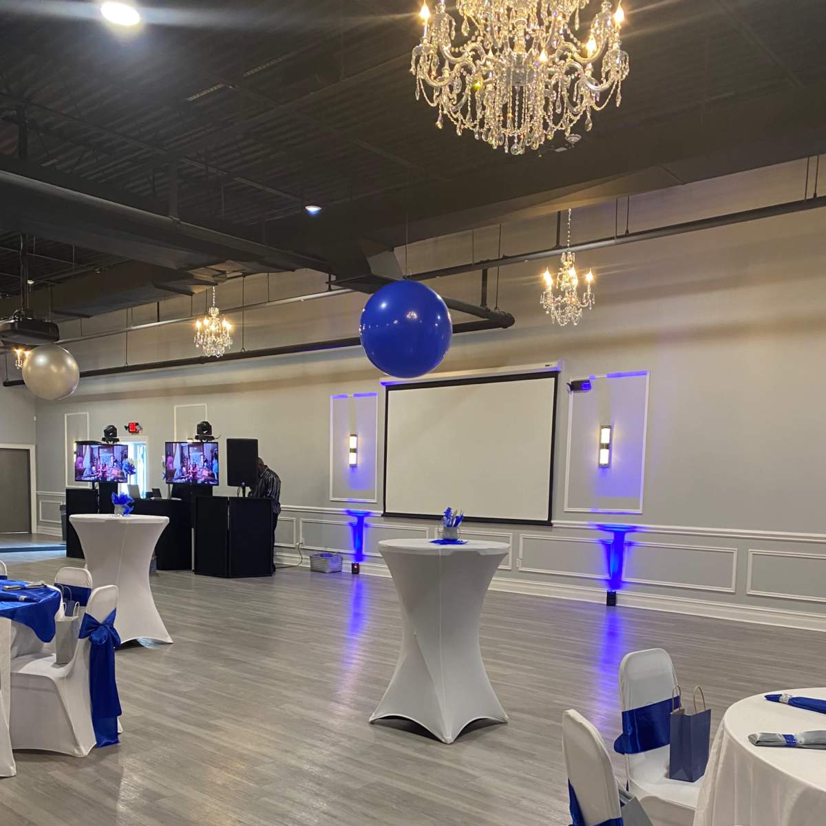 A banquet hall set up for an event, featuring tables with blue decorations and a large screen at the front.