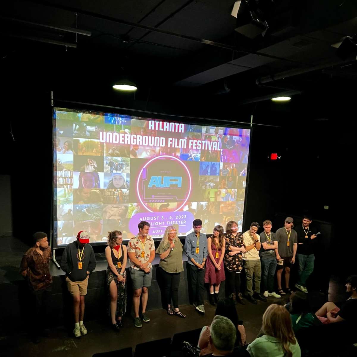 A group of individuals stands in front of a large screen displaying the logo and details of the Atlanta Underground Film Festival.