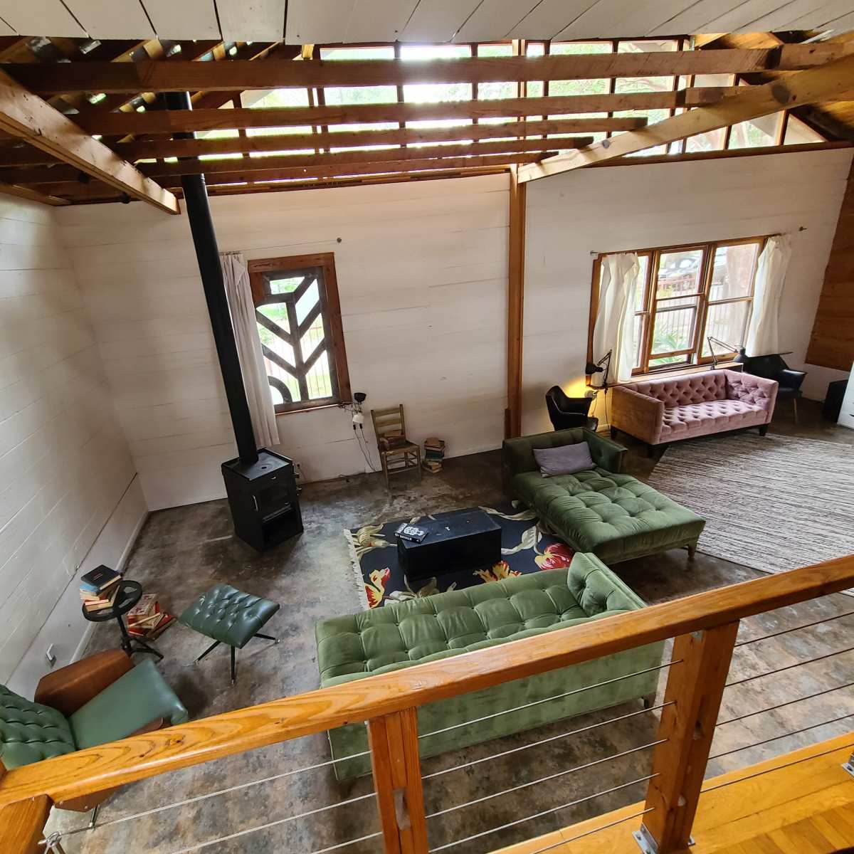 A spacious living area with green sofas, a wood stove, and large windows, featuring a mix of wood and concrete flooring.