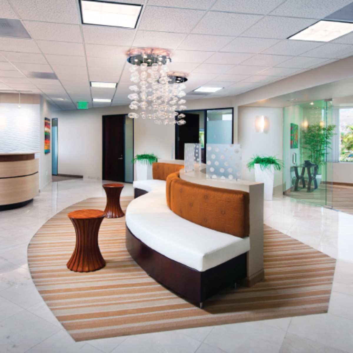 A modern reception area with white seating, a wooden accent table, and chrome light fixtures, set on glossy marble flooring.
