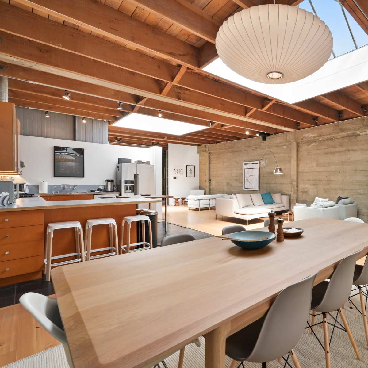 A spacious, modern open-concept living and dining area with wooden beams, a large dining table, and a bright seating area.