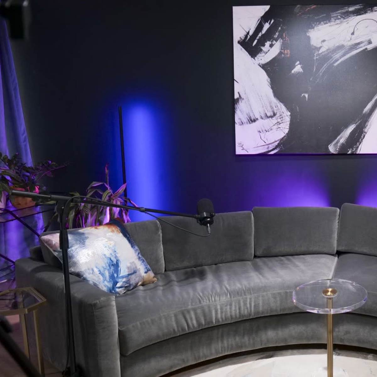 A modern living room features a curved gray sofa, a glass side table, and an abstract painting on the wall, with decorative lighting creating a contemporary atmosphere.