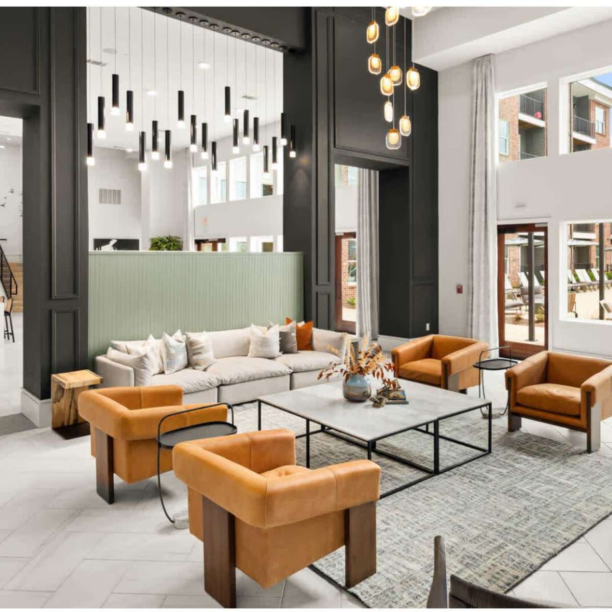 A modern, spacious lobby area featuring orange armchairs, a large coffee table, and panoramic windows overlooking a pool area.