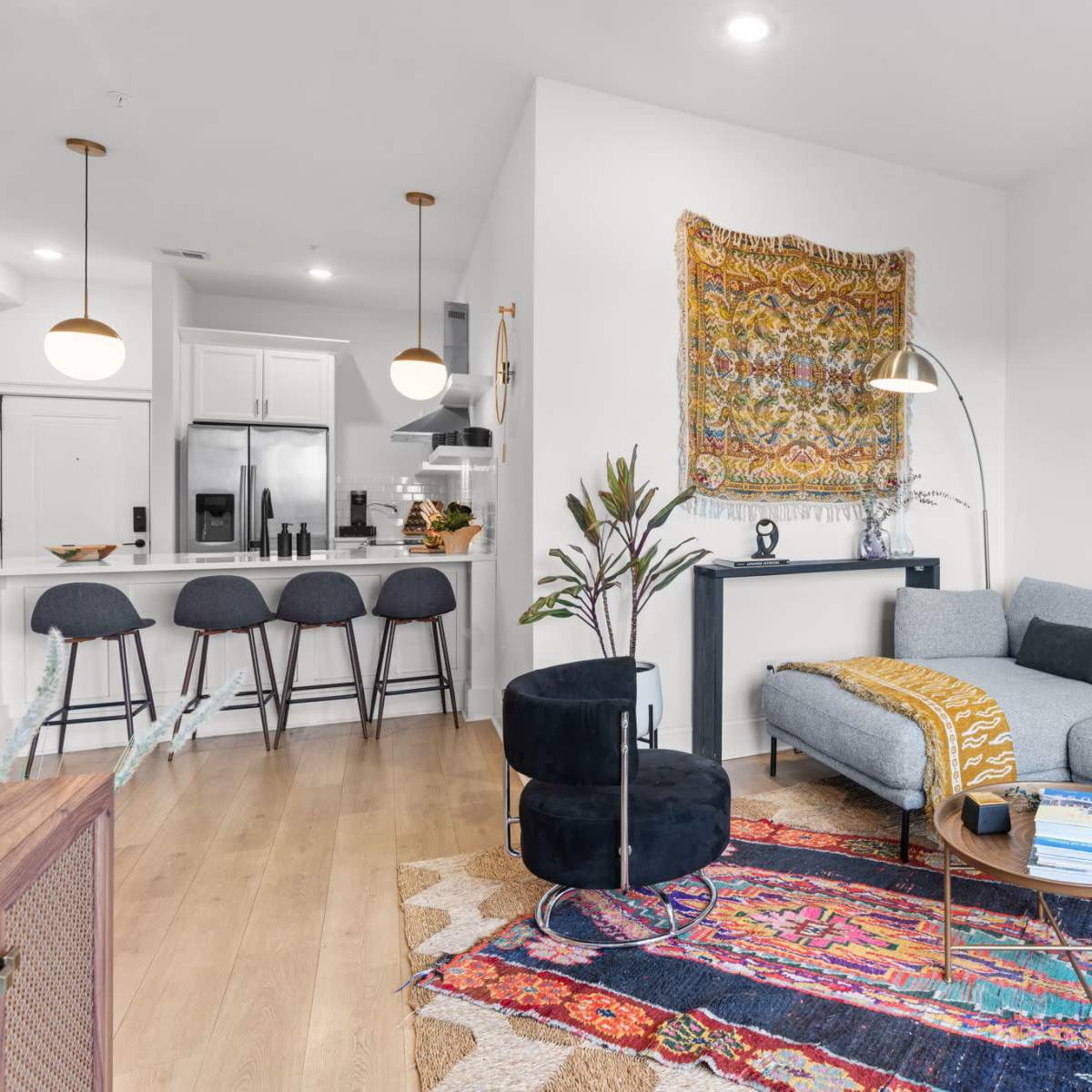 A modern living room with a gray sectional sofa, a round coffee table, decorative wall art, and a kitchen area in the background with bar stools.