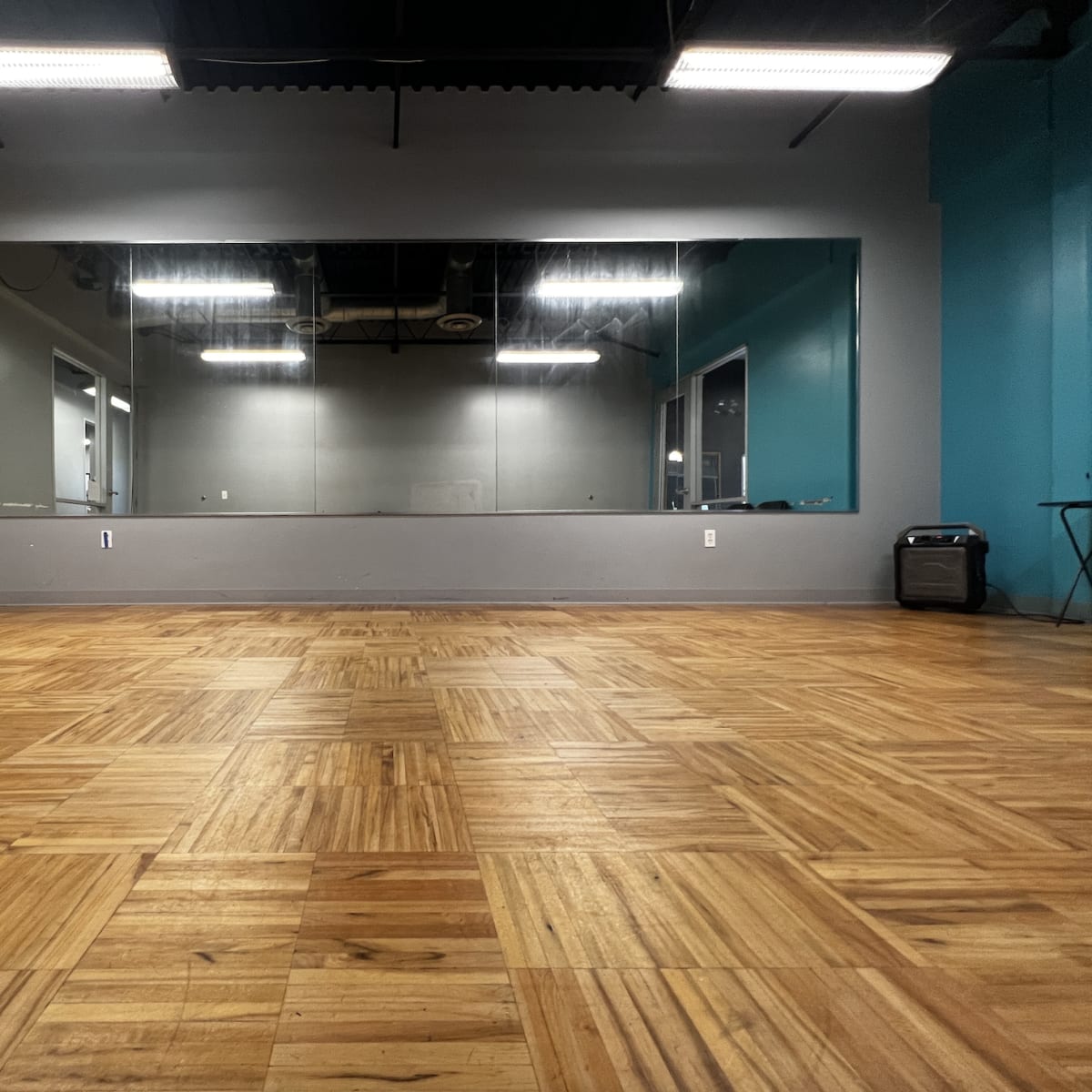 A spacious room with polished wooden flooring, large mirrors on one wall, and a blue accent wall opposite the mirrors.