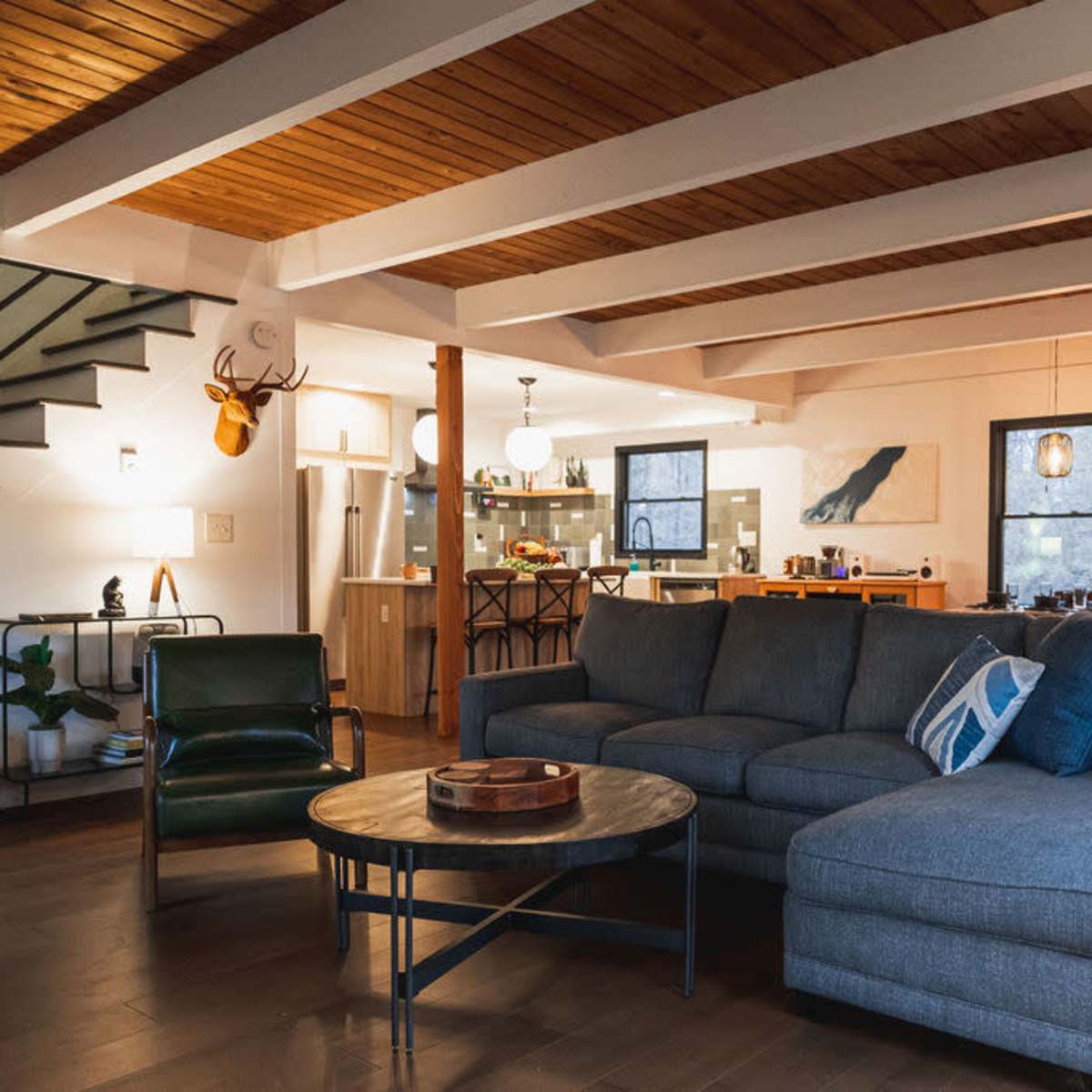 A modern living room with a large sectional sofa, a coffee table, and an open layout connecting to a kitchen area.