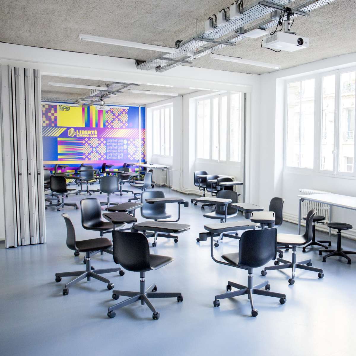 A modern classroom with multiple black chairs and tables arranged in a spacious, brightly lit room.