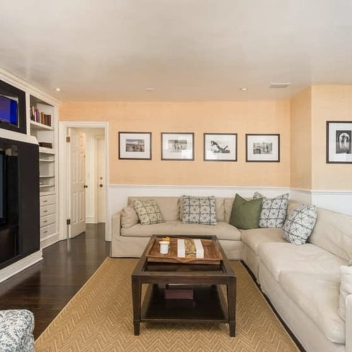 The living room features a large sectional sofa, a coffee table, and framed black-and-white photos on the walls, with a television mounted above a console.