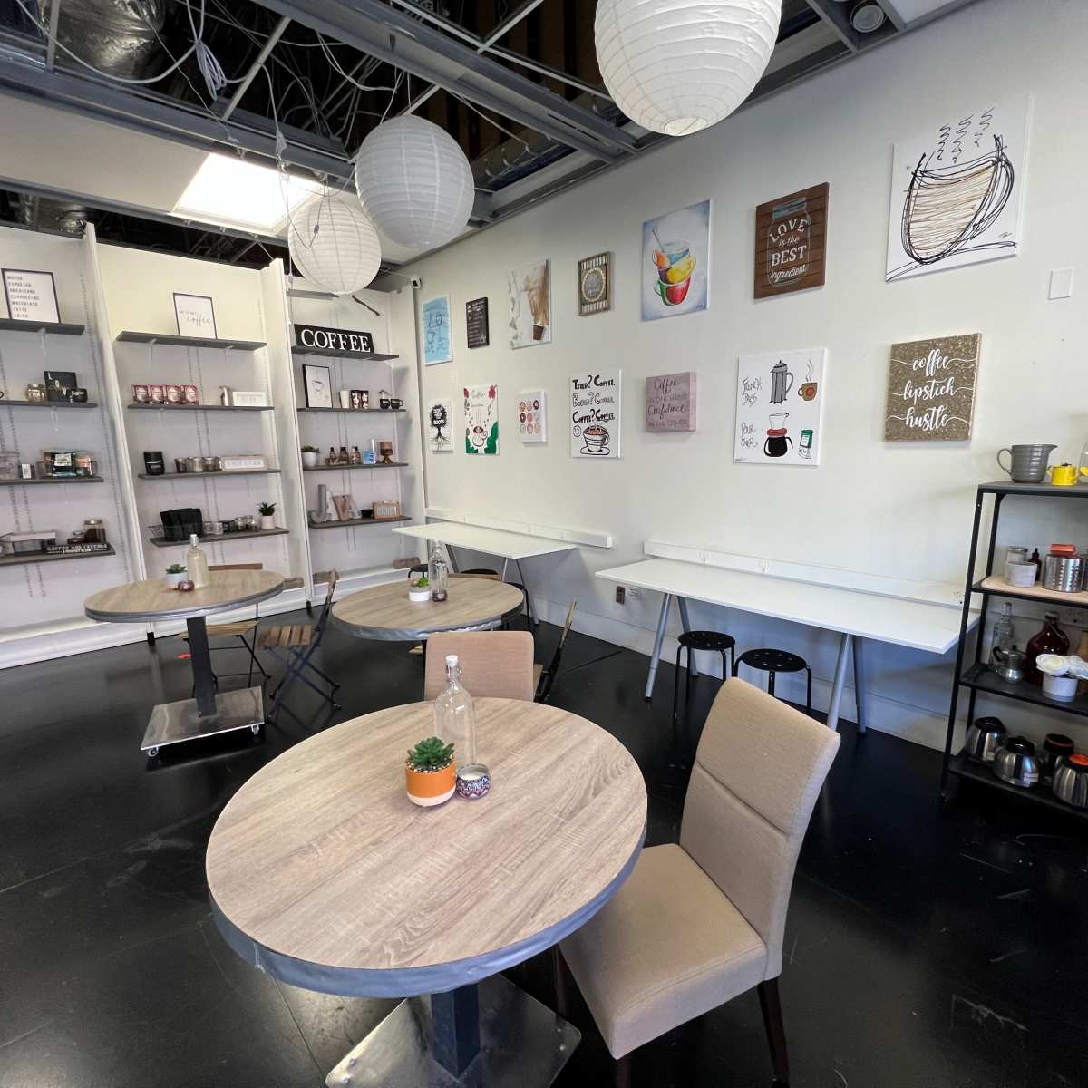 A modern café interior with wooden tables, chairs, and wall art featuring coffee-related themes.
