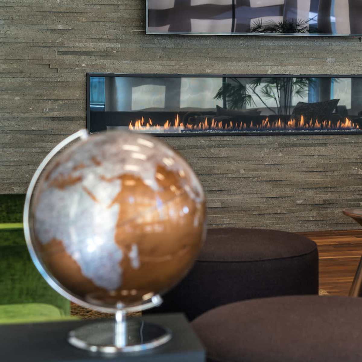 A modern living space featuring a linear fireplace mounted on a stone wall, with a globe and seating arrangements in the foreground.