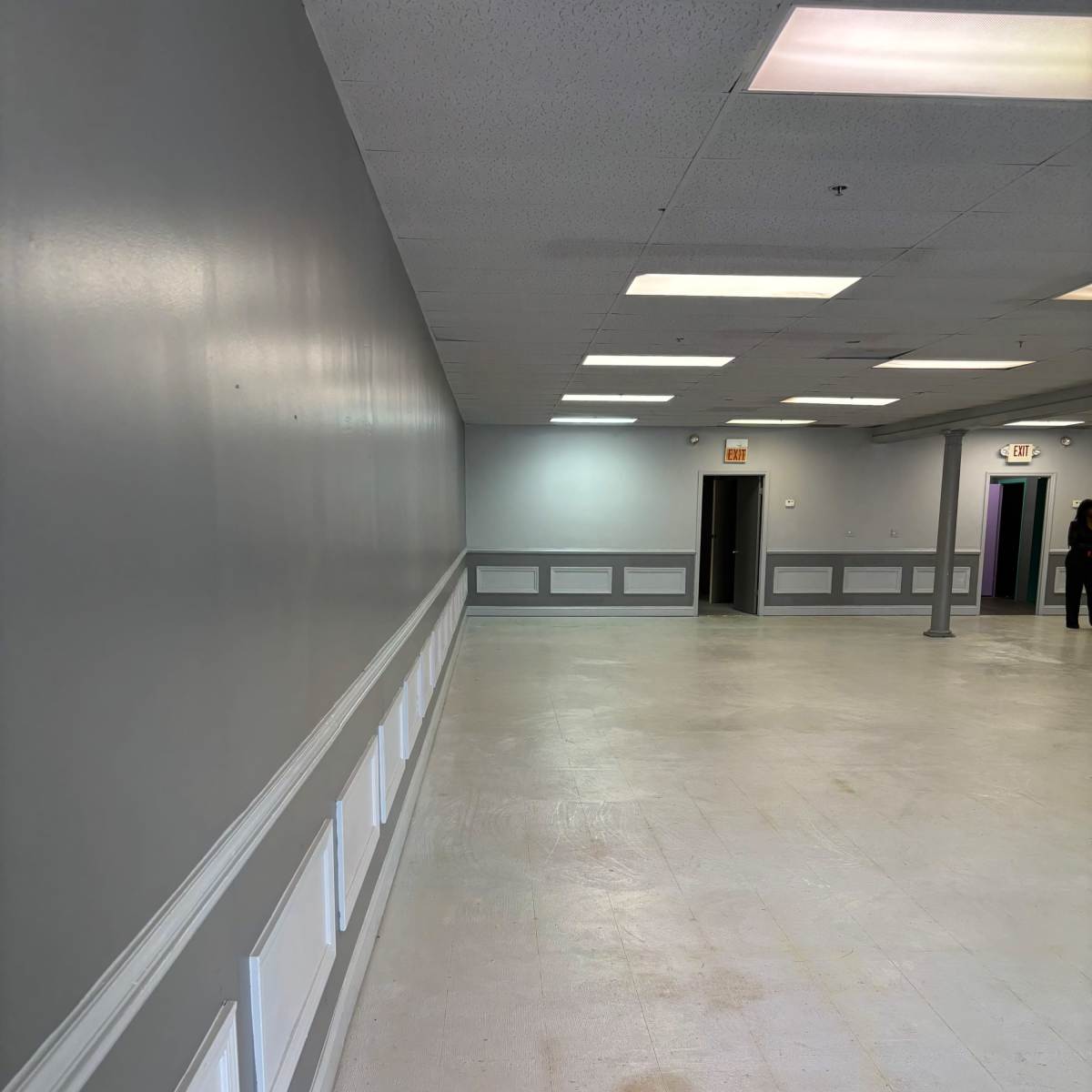 An empty room with gray walls, white trim along the base, and fluorescent lighting.