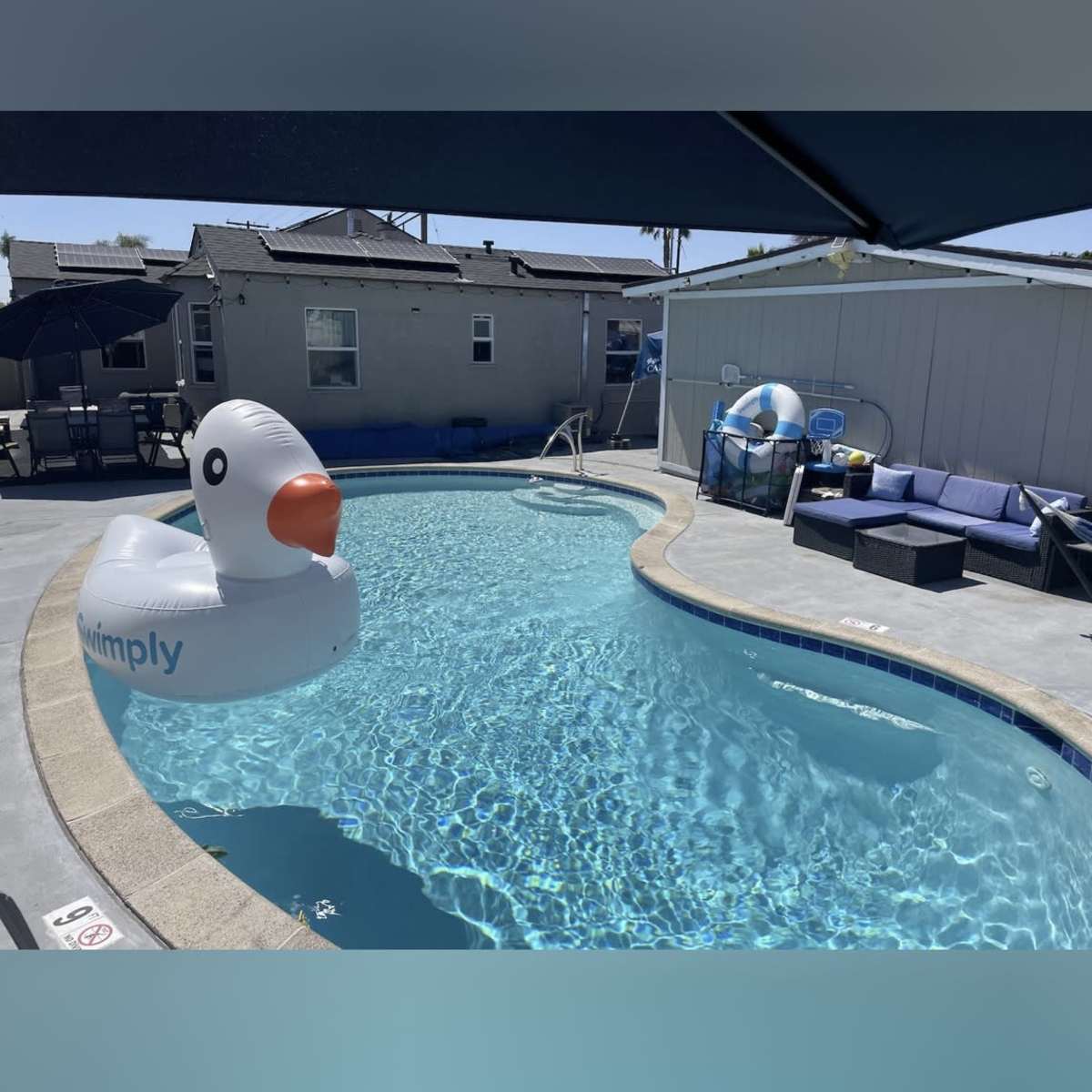 A large inflatable duck floats in a swimming pool surrounded by lounge furniture and a covered seating area.