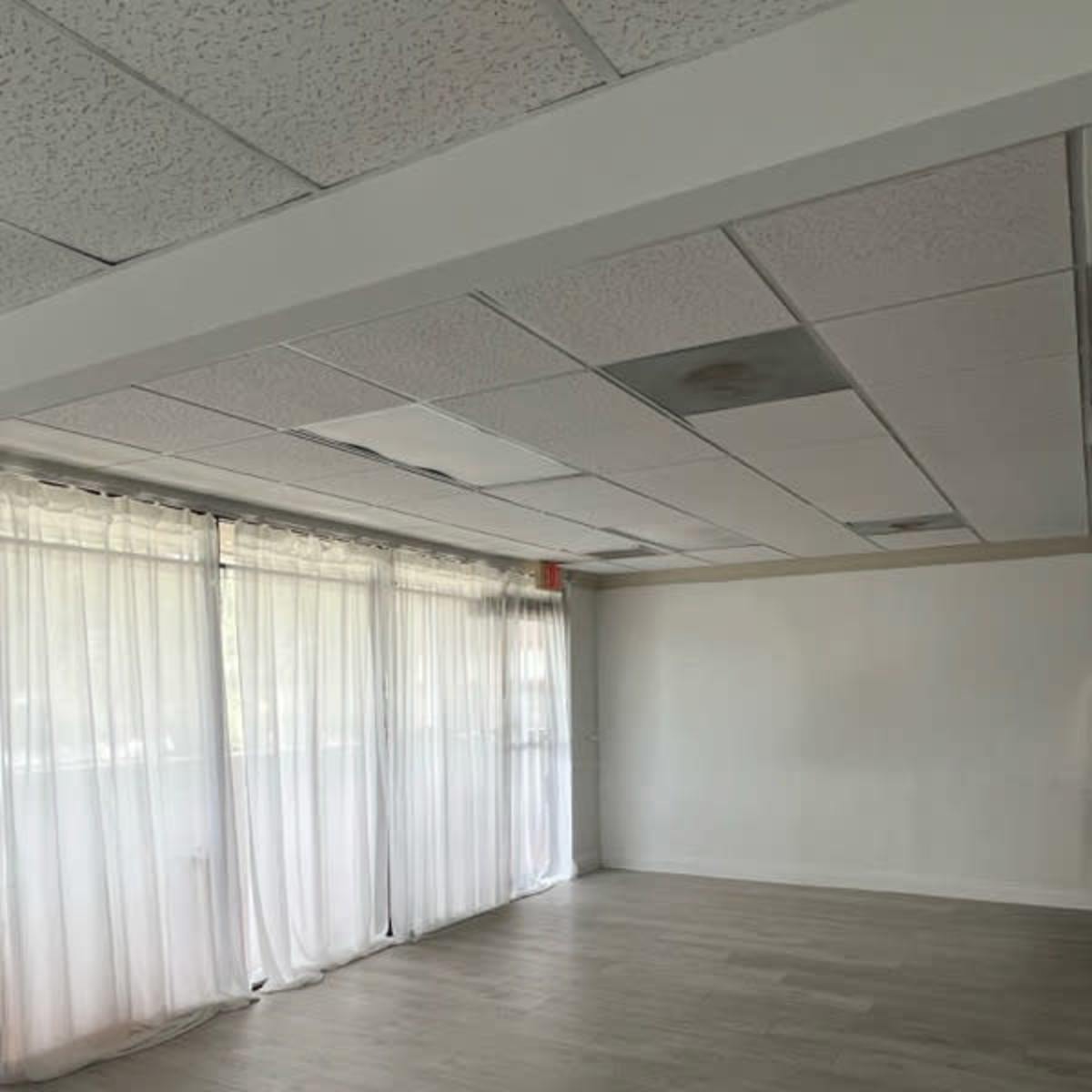 An empty room features large windows with sheer curtains and a light-colored floor.