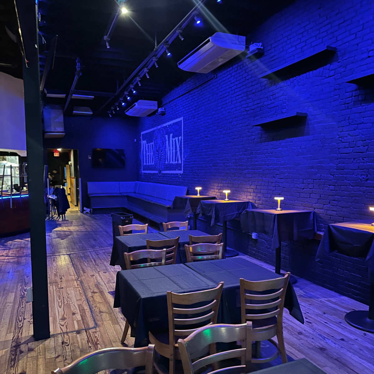 A dimly lit restaurant or bar with blue lighting, featuring several tables covered in black cloth and a wall displaying the word "Mix."